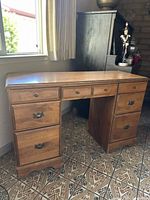 Front-left angle view of wooden desk showing three top drawers and left pedestal drawers