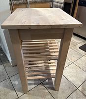 Side view of butcher block kitchen island showing butcher block surface top and slatted shelves beneath with solid wood square legs.