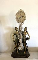 Full view of the goddess quartz pendulum figural clock on a neutral background showing the clock face, pendulum, and detailed two goddess statues.