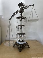 Front view of the Hollywood Regency-style balance scale showing the metal frame, decorative glass plates, crystal bead accents, and marble base.