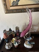 Full view of the pink Murano glass fish sculpture surrounded by ceramics and the prayer candle on a table against a textured wall.