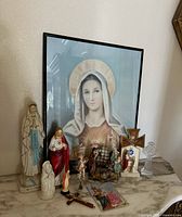 Full frontal view of the religious iconography collection on a marble surface including framed Virgin Mary print and various statues and crosses