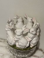 Front angled view showing detailed white ceramic bunnies on green base above clear cut glass bowl.