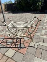 Photo of white metal garden bench showing curved legs and scrollwork, placed outdoors on patio.