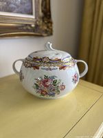 Front view of large vintage T. Limoges porcelain soup tureen with floral designs and lid on a yellow table.