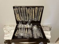 Open wooden case showing top row of wrapped knives and forks