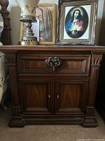 Photo showing a vintage wooden nightstand by Drexel with drawer and cabinet doors, ornate handles, carved details, and dark wood finish.