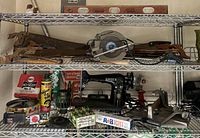 Shelves containing a vintage Singer sewing machine, Black & Decker circular saw, hand saws, levels, cans of lubricants and epoxy putty, and various hardware tools.