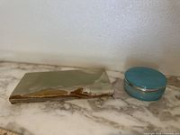 Photo of blue alabaster trinket box with silver rim next to rectangular onyx slab on marble surface