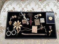 Top-down view of vintage jewelry lot displayed on black velvet tray, showing brooches, earrings, pendants, rosary, and bracelet with clear details.