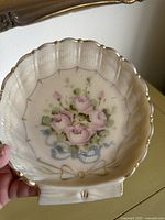 Close-up of pink milk glass dish by Cambridge Crown Tuscan featuring pink rose floral design with blue ribbons and gold trim on scalloped edges.