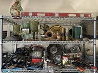 Wide view of the shelf containing vintage car parts, metal items, glassware, and tools