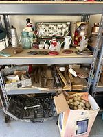 Shelf with various vintage Christmas decorations including ceramic snowmen, Santa figurines, glass jar, small candles, and metal and wooden household items.