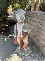 Photo of vintage concrete hobo statue outdoors, showing front angle with visible wear and painted details
