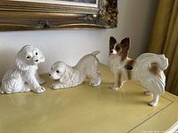 Three ceramic dog statues: two small white dogs (sitting and crouching) and one larger brown and white dog with Coopercraft label.