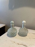 Pair of small hobnail textured glass bottles with matching rounded stoppers displayed on a white surface against a neutral wall.