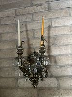 Front view of the ornate gilt bronze wall sconce holding two taper candles with crystal pendants.