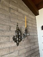 Side view of vintage gilt bronze neoclassical wall sconce with a yellow taper candle, mounted on a brick wall.