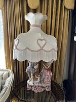 Full view of lamp on round glass-top table showing base figurines and shade.