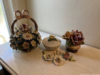 Photo showing entire set of ceramic flower basket, lidded basket, rose figurine, and small flower pieces on a marble surface near window light.