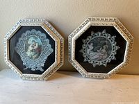 Pair of octagonal framed artworks with romantic scenes and lace-like frame details shown side by side on a light surface against tan wall.