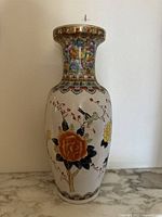 Front view of large vintage ceramic vase with pink, orange, and yellow flowers and bird motifs on white base