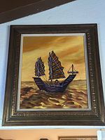 Photo of a vintage large framed painting of a traditional ship on water with warm yellow and orange colors, signed by the artist at bottom right.