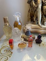 Angle showing eight vintage miniature perfume bottles with varied shapes and designs on a decorative surface near gilt sculpture