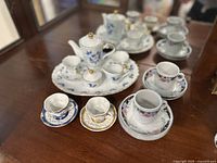 Overall view of the vintage miniature porcelain tea and coffee set arranged on a glass surface.