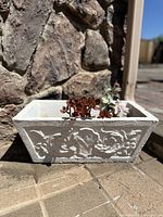 Side view of rectangular off-white concrete planter with floral relief, showing texture and detailing.
