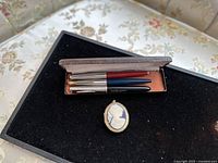 Four Parker pens in a vintage box with a carved cameo pendant on black surface