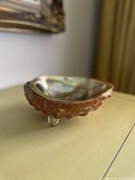 Angled side view of the bowl showing the red abalone shell exterior and lucite feet.