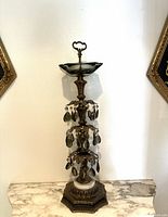 Full view of the vintage brass standing ashtray with smoky glass hanging prisms and hexagonal base on a marble surface against white wall.