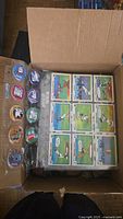 Open box with clear plastic sheets holding a variety of Looney Tunes and Batman collectible pogs with colorful cartoon designs.