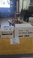 Two white cardboard storage boxes labeled as Donruss 1994-95 and 1996-97 hockey card sets with handwritten text on the boxes and a note indicating 45 total boxes or cards.