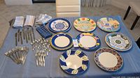 Full layout of eclectic dinner plates, cloth napkins, and flatware on blue tablecloth