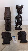 Four Nigerian ebony carvings on floor, showing variety and detail of each statue with measuring tape and lot tag.