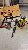Wide shot of lot including Shop-Vac, Workmate 200 foldable workbench, garden stakes, push broom, and shovel arranged on concrete floor