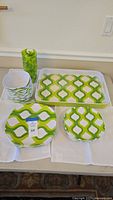 Full view of the serving set with stack of plates, bowls, cups, and tray all in green geometric melamine pattern.
