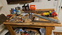 Overview photo showing a collection of small hand tools, motor oil, and other hardware items on a wooden table.