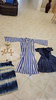 Four pieces of vintage African clothing displayed on floor: child's Egbada outfit with hat, adult blue and white striped robe, tie-dye skirt, and dark blue patterned dress/robe.