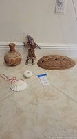 Photo of the full lot including pottery vase, witchdoctor doll, carved wooden wall hanging, shell necklace, and sea urchin arranged on floor.