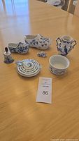 Photo showing entire lot of ceramic Delftware pieces including two Dutch shoes, bell, teapot lid, two-handled vase, small bowl, and miniature shoe.
