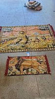 Photo showing both tapestry rugs, larger featuring The Sphinx with figures and pyramids, smaller showing lion with fringed edges.