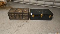 Pair of vintage storage trunks on concrete floor, showing side by side comparison and overall condition.