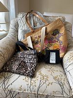 Four tote and purses on upholstered chair: two canvas fish print totes, leopard print purse, and boxed black crossbody bag