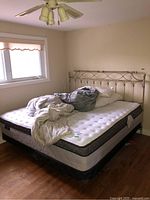 Full side view of king size bed with mattress and linens, showing thickness of mattress and metal headboard design.