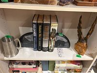 Shelf with four hardcover fiction books, two pewter tankards, two stone bookends, and a wood carved wings piece shown together