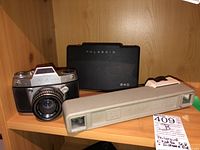 Lot items displayed on wooden shelf: Exakta 500 camera, Polaroid 240 case, and Jessop Dresden distance finder.