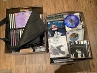 Photo showing two cardboard boxes filled with various CD jewel cases and some paper sleeves. Cyndi Lauper album "At Last" visible on top of one box.